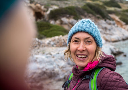 A cheerful, joyful blonde in a knitted hat laughs, standing on the seashore. travel to turkeyの写真素材