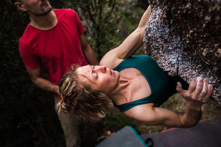 strong girl climb bouldering with friends in nature. rock climbing in nature as fitness and sports. overcoming a difficult route with the help of friends and their support.の写真素材