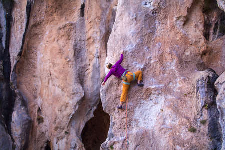 A girl trains strength and endurance on rocks, climbing on natural terrain, a rock climber overcomes a difficult route, an active lifestyle. rock climbingの写真素材