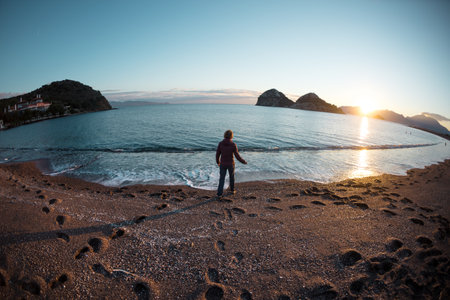 girl walks along the seashore at sunset time. a walk along the sandy beach alone. loneliness and freedom concept.の写真素材