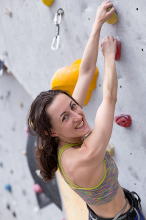 Smiling girl climbs the climbing wall, the woman is engaged in extreme sports, rock climbing in the city, strength and endurance trainingの写真素材