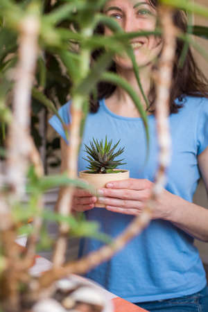A woman holds a pot of succulent in her hands, a girl sells flowers, growing plants for sale, a plant as a gift, flowers in a greenhouse, potted plant.の写真素材