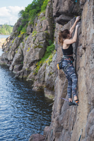 A girl climbs a rock above the water, a woman is engaged in extreme sports, rock climbing on natural...