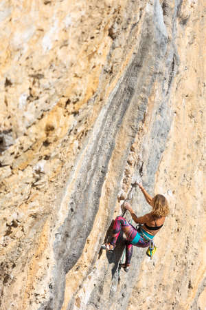 The girl climbs the rock. The climber trains on natural terrain. Extreme sport. Outdoor activities. A woman overcomes a difficult routeの写真素材
