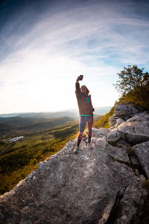 The girl takes a selfie on the top of the mountain during sunset. travel the mountains. girl taking picturesの写真素材
