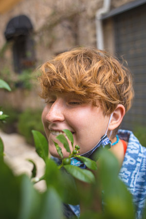 Portrait of a girl in a mask sniffing flowers, a walk in a spring park, a red-haired woman feels the aroma of spring flowers, flowering treesの写真素材
