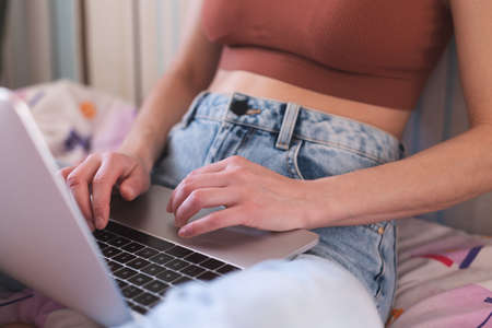 A girl works from home, female hands on a laptop keyboard close-up, a woman sits on a sofa with a laptopの写真素材