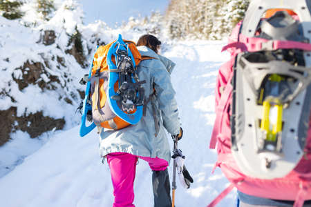 Two women walk with snowshoes on the backpacks, winter trekking, two people in the mountains in winter, hiking equipmentの写真素材