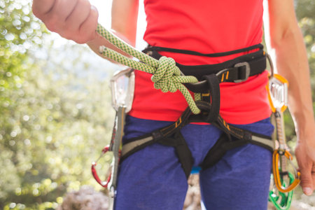 A girl rock climber ties herself with a rope to the harness for safe climbing in the mountains....