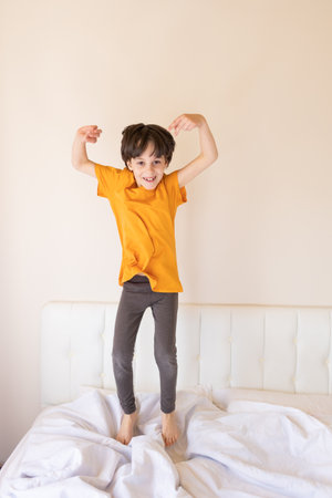 An energetic child is jumping on the bed, a boy in pajamas is fooling around in his room, the child is enjoying the weekendの写真素材