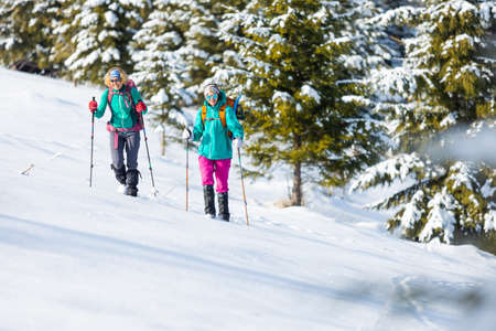 Two women walk through the snow on a winter hike, two in the mountains in winter, hiking equipment, snowshoesの写真素材