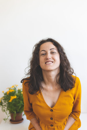 A woman and a pot with a flowering plant, a smiling girl in a yellow dress sits against the...