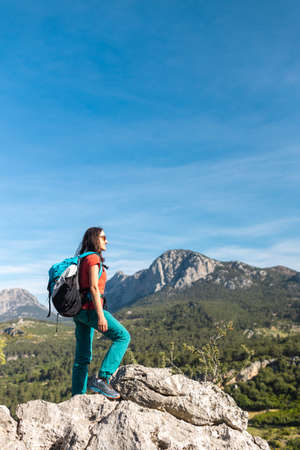 A young woman with a backpack climbed to the top of the mountain and looks at the valley, hiking in the mountains, success in achieving the goalの写真素材