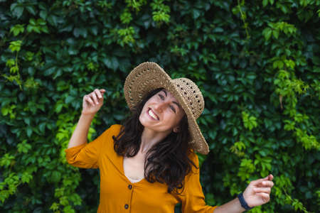 A smiling girl in a straw hat stands near a wall overgrown with ivy, a portrait of a woman with dark hairの写真素材