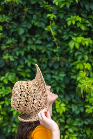 A smiling girl in a straw hat stands near a wall overgrown with ivy, a portrait of a woman with dark hairの写真素材