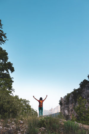A young woman with a backpack climbed to the top of the mountain and looks at the valley, hiking in...
