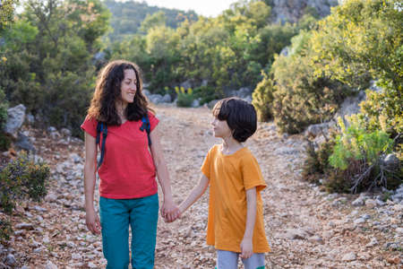 Mom with a child walk in the park, a woman spends time with her son, mother's day, a boy walks with his mother in the forest, woman holding her son's handの写真素材