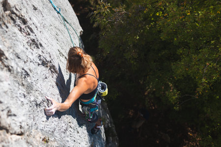 girl rock-climber climbs the rock against the background of the autumn forest and blue sky. a...