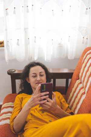 A girl in a yellow dress lies on a sofa and holds a smartphone in her hands, a woman rests at home...