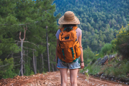A woman with a backpack and a straw hat in the forest, a smiling girl on a hike, summer trekking, happy woman enjoying her walk on a mountain pathの写真素材