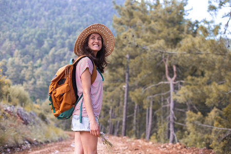 Portrait of a woman with a backpack and a straw hat in the forest, a smiling girl on a hike, summer...