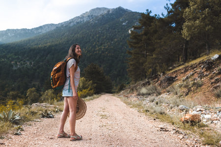 A woman with a backpack on a mountain path, a hike in the mountains, a girl in a hat walks along a...