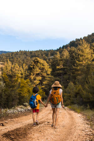 A child with mom walks in the woods, a woman travels with a child, a boy with mother walks along a forest path, a child with a backpack on a hikeの写真素材