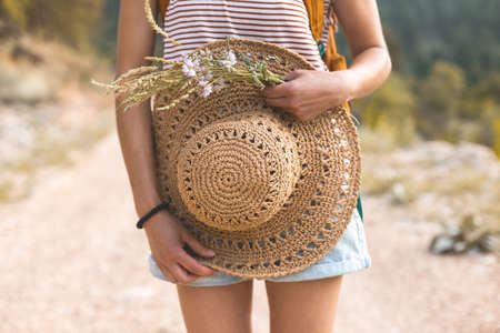 The girl holds in her hands a straw hat and a bouquet of wild flowers, summer accessoriesの写真素材