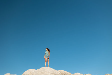 the girl stands against the background of the blue sky. joyful young girl stands on top of the...