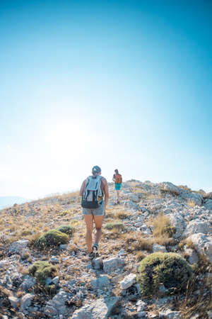 two girls with backpacks walk along a mountain path. trekking and vacation adventure. climbing and freedom.の写真素材