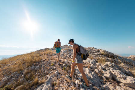two girls with backpacks walk along a mountain path. trekking and vacation adventure. climbing and freedom.の写真素材