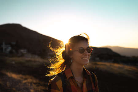 portrait of a beautiful young girl in glasses on a walk in the mountains. travel in the mountains at sunset. happiness and freedomの写真素材