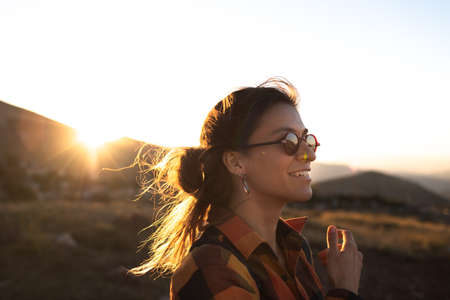 portrait of a beautiful young girl in glasses on a walk in the mountains. travel in the mountains at sunset. happiness and freedomの写真素材