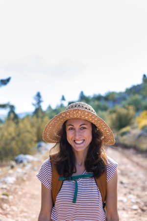 Portrait of a woman with a backpack and a straw hat in the forest, a smiling girl on a hike, summer...