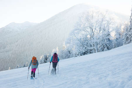 climbers climb the mountain. two girls in snowshoes walk in the snow. hiking in the mountains in winter.の写真素材