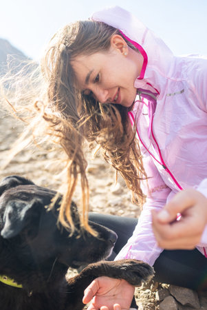 a young woman plays with a black dog on a background of mountains. girl with a dog. travel and freedom conceptの写真素材