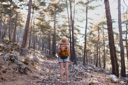 Portrait of a woman with a backpack and a straw hat in the forest, a smiling girl on a hike, summer trekking, happy woman enjoying her walk on a mountain pathの写真素材