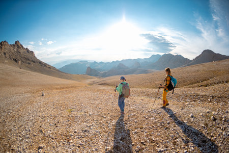 two girls on a walk in the mountains. young girls with backpacks walk along a mountain path against the sky.の写真素材