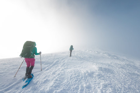 two girls walk along a mountain path in snowshoes. walking in the snow. hiking in the mountains in...