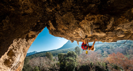 Girl climber on an overhanging rock. A sports woman climbs a rock against the backdrop of mountains....