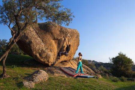 A strong girl climbs a large boulder, bouldering on natural terrain, friends are climbing in Turkey, a large boulder in the park, friends support, gymnastic belayingの写真素材