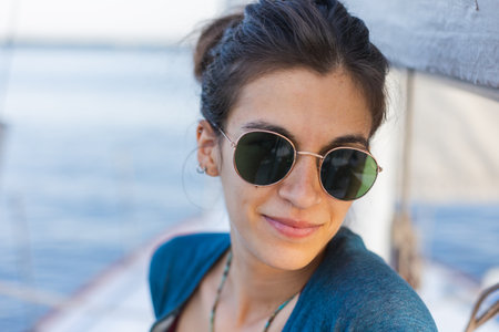Happy smiling portrait of a beautiful young girl in sunglasses on a yacht or boat on the coast with the sea in the background. paradise island cruiseの写真素材
