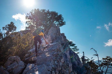 The girl is climbing the rock. Woman climber with a backpack and a helmet in the mountains. adventure and mountaineering concept. hiking with a backpack in the mountains. mountains of Turkey.の写真素材