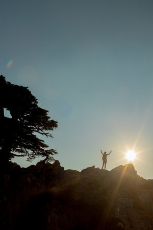 Silhouette of a girl with a backpack on a rock at sunset. The silhouette of the winner on the top of the mountain. The concept of sports and active life. travel in the mountains.の写真素材
