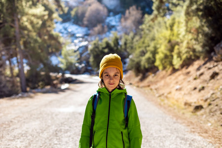 A boy with a backpack in the middle of a forest road, a child is exploring wildlife, a child is standing alone among the trees, a portrait of a boy. Travel and hiking.の写真素材