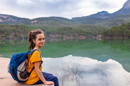 A child with a backpack looks at a beautiful mountain lake. Relaxed, peaceful, thoughtful, happy and free on a mountain lake. vacation with childrenの写真素材