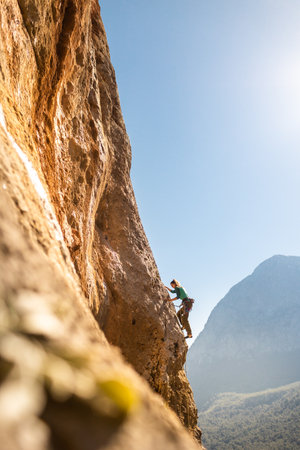 The girl climbs the rocks against the background of the sky and mountains. sports girl is engaged in rock climbing. extreme sportsの写真素材