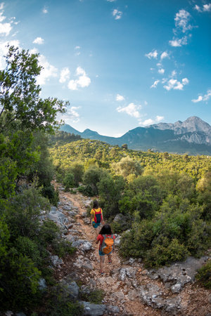 Two girls with a backpack walk along a mountain road, women against the backdrop of a beautiful mountain and sky, a journey through the beautiful places of the world, travel to Turkeyの写真素材
