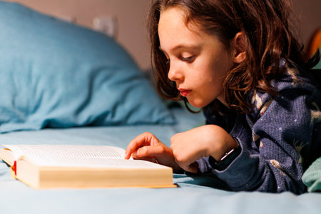 child reads a book before going to bed. Children's book to read in bed. children read books. children's room. Little curly boy in pajamas at home.の写真素材