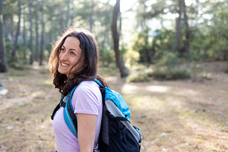 A young girl with a backpack travels through the forest. Tourist hike in the forest and mountains. The girl smiles at the camera. hike and adventure concept.の写真素材